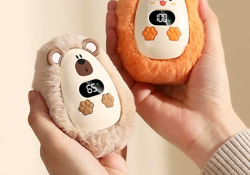 Dos calentadores de manos CozyPuff sujetados en las manos, mostrando temperatura y batería